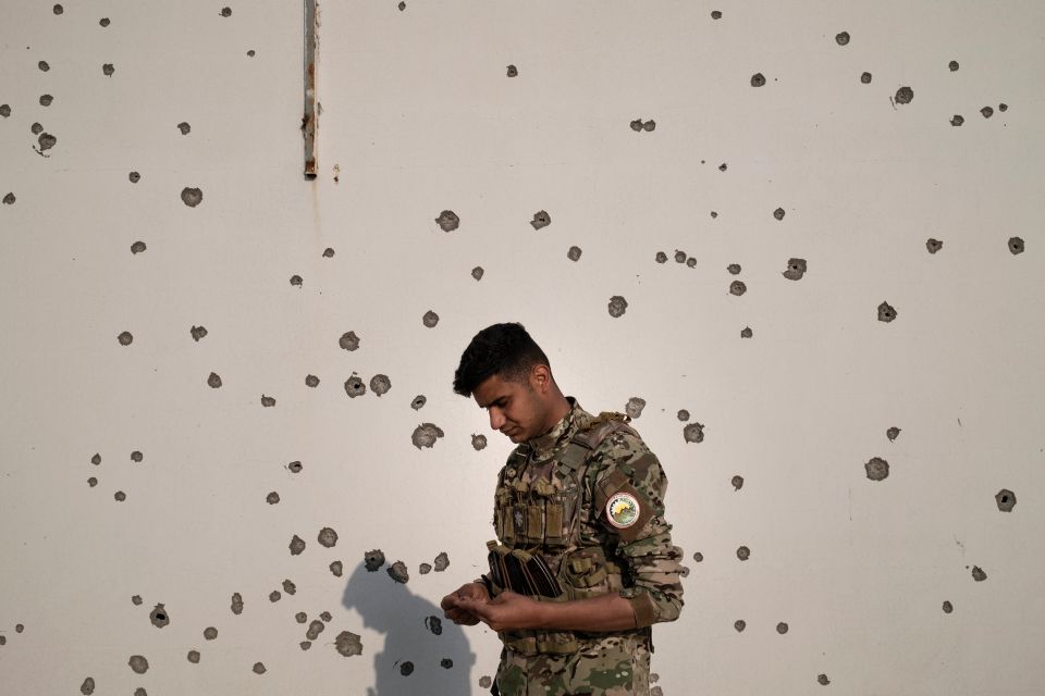 Portraitfoto von Saman in Kampfmontur vor einer Wand mit Einschusslöchern