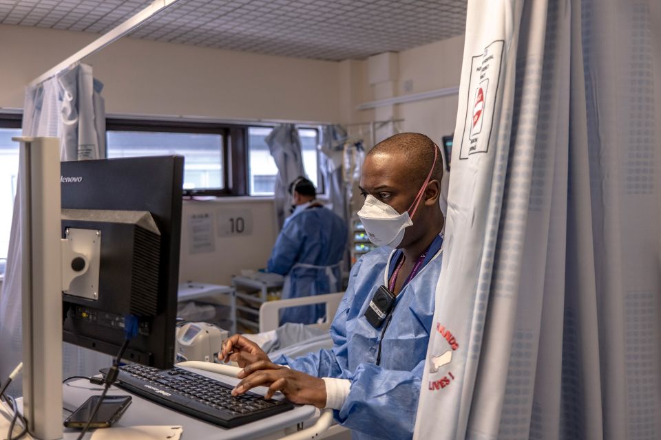 ein Pfleger mit Maske tippt sitzt vor einem Computer