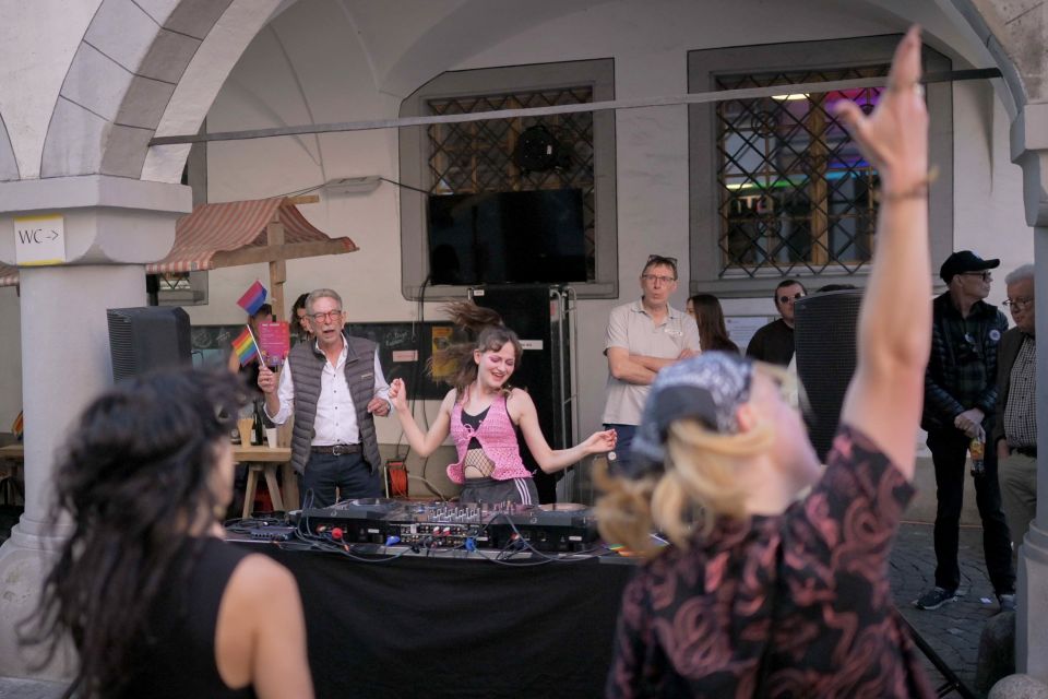 eine Discjockey steht an einem DJ-Pult, davor und daneben feiern Menschen