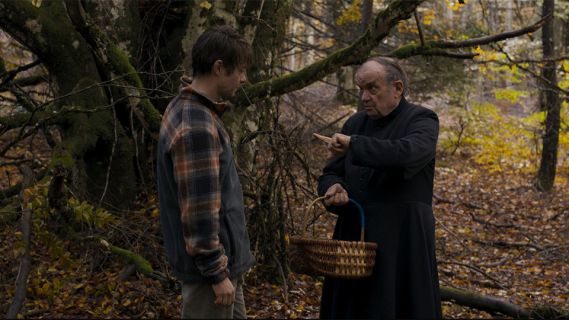 Filmstill aus «Miséricorde»: der Dorfpfarrer redet mit einem Mann im Wald