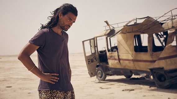 Filmstill aus «Sirāt»: ein Mann steht neben einem zerstörten Kleinbus in der Wüste