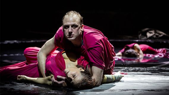 Bühnenfoto des Theaterstück «Die Orestie»: ein Mann hält eine Frau in den Armen, welche auf dem Boden liegt