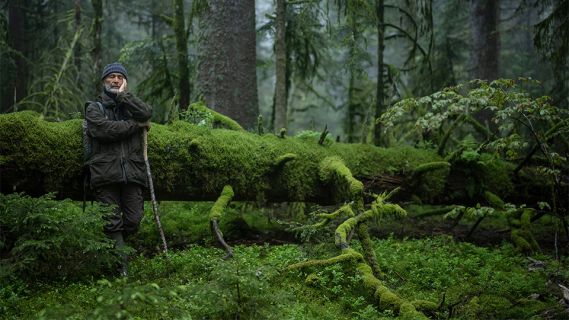 Filmstill aus «Le chant des forêts»: ein Mann mit einem Stock steht im Wald mit geschlossenen Augen